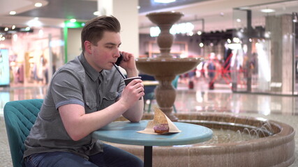 A young man in a cafe speaks on the phone against the background of a fountain. Decoration in the cafe.