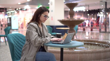 Young woman in a cafe with a laptop on the background of a fountain. Decoration in the cafe.