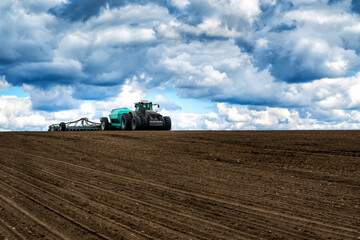 Naklejka premium sowing work in the field in spring. Tractor with seeder
