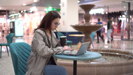 Young woman in a cafe with a laptop on the background of a fountain. Decoration in the cafe.
