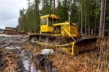 Logging in the forest. Yellow tracked forestry tractor. Dirty forest road, logs in the background.