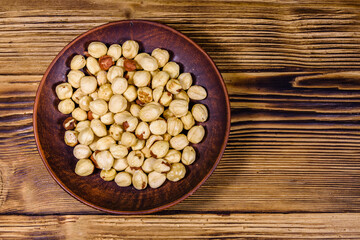 Ceramic plate with peeled hazelnuts on a wooden table. Top view