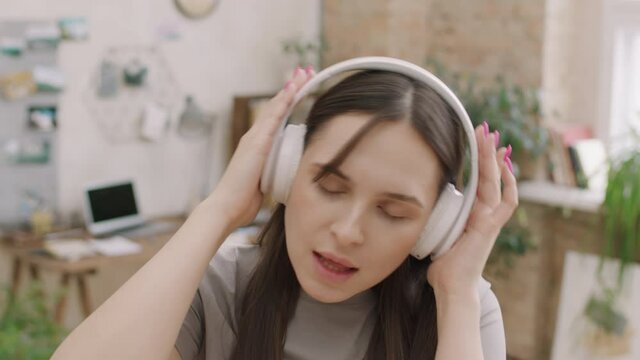 Close up shot of young woman in headphones singing and moving to music before camera