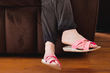 Female bare feet in pink sandals while relaxing on couch or sofa.