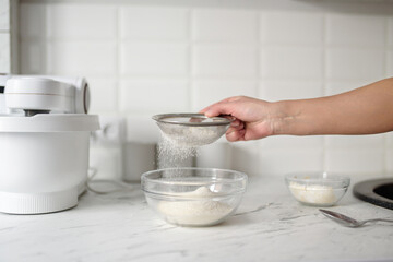 Fototapeta na wymiar Women's hands sift flour through a sieve.Close-up