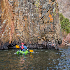 senior male kayaker is paddling a whitewater inflatable kayak on a mountain river in early spring -...