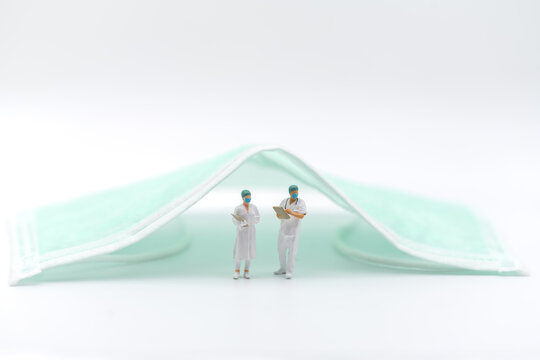 Healthcare and Protection concept. Closeup of doctor and nurse miniature figure people with patient files and standing under surgical face mask on white background.
