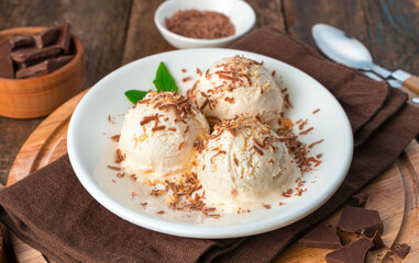 Three balls of ice cream close-up in a white plate on a brown background.