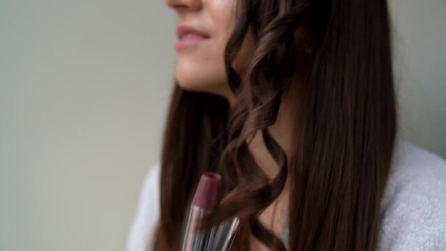 Closeup of female hands are holding curling iron. Young smiling woman girl is twisting hair, making curls after washing, doing hairstyle. Tools and devices for styling. Personal hygiene and care.
