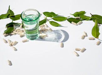 A glass of water. Capsules are scattered and green leaves. Alternative medicine and nutraceutical topics. Copy space for text.