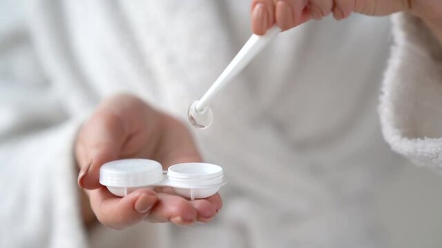 Closeup female hands are holding plastic container for contact lenses. Woman is washing soft optical lens in cleaning liquid, preparing to put in eye. Vision correction of myopia, hyperopia concept.