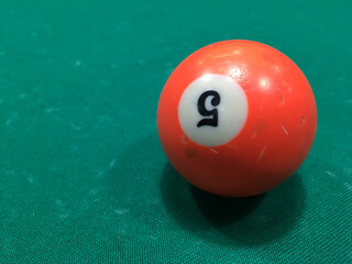 Orange billiard ball on green scratched fabric of a billiard table