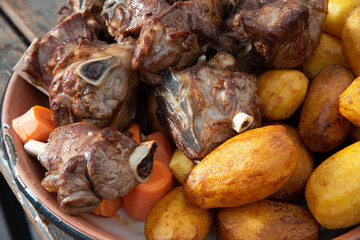 roast lamb meat with potatoes and carrot in a big plate on a wooden table
