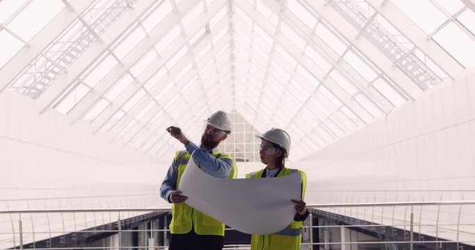 Male civil engineer and female architect standing inside new business office center, holding building plan drawing, discussing details. Engineers working at construction site.