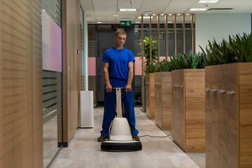 Cleaning worker in a blue uniform polishing floor in an office