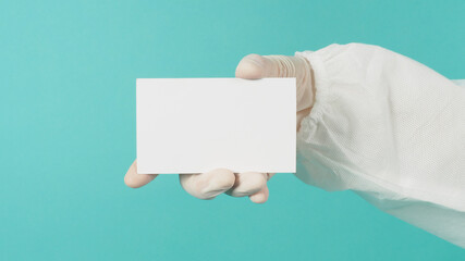 Blank white card board in woman's hand.She wear latex glove andPPE suit on green mint or Tiffany...