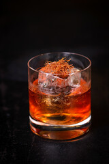 Negroni with big ice cube and saffron on top in vintage glass with dark background. Late night drink concept.