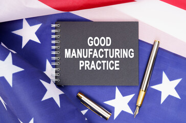 On the table is an American flag, a pen and a notebook with the inscription - GOOD MANUFACTURING PRACTICE