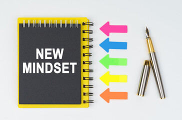On a white background lies a pen, arrows and a notebook with the inscription - NEW MINDSET