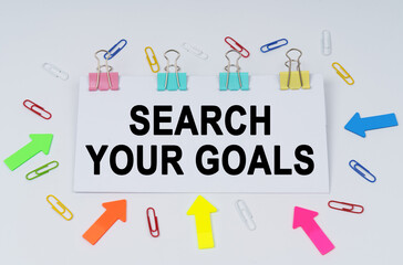 On the table there are paper clips and directional arrows, a sign that says - Search Your Goals