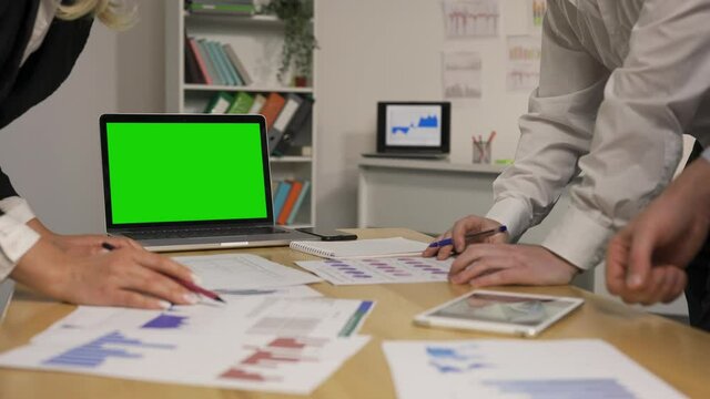 Business partners discussing economic situation of company at meeting. Group viewing papers with charts and graphs. Laptop with green screen chroma key. Close up. Slow motion ready, 4K at 59.94fps.