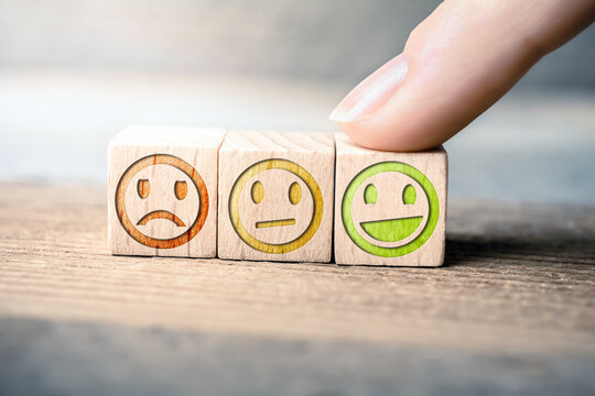 Good Feedback Concept With Red, Yellow And Green Smileys On Wooden Blocks On A Board, The Green Smiley Is Touched By A Finger