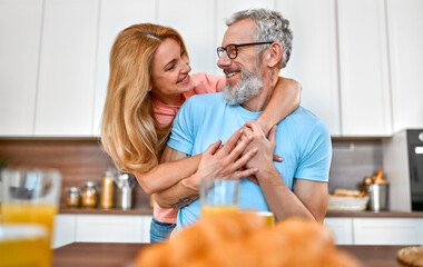 Fototapeta na wymiar A mature married couple hugs and has breakfast in the kitchen early in the morning and has a good time romantically.