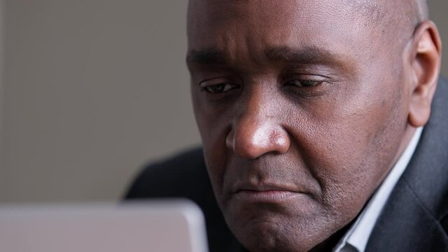 Close-up focused male wrinkled face looking at laptop screen, african mature business man uses computer in office reading news email online emotionally raising eyebrows, 40s afro boss working on net.
