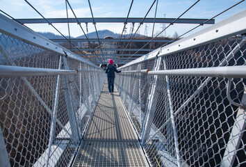  girl in a blue jacket and pink hat walks on a suspension bridge in Sky Park