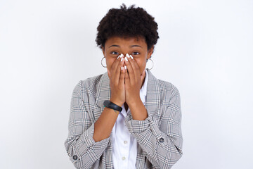 Vivacious African American businesswoman with curly bushy hair wears  formal clothes over white background, giggles joyfully, covers mouth, has natural laughter, hears positive story or funny anecdote