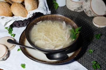 chicken noodle soup in brown bowl with spoon and bread on a background