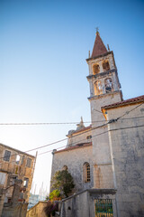 Fototapeta premium Bell tower of the Church of Our Lady of the Annunciation at the end of a narrow street in the town of Milna on Brac island, Dalmatia, Croatia
