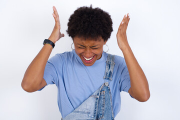 African American female with afro hair wears jeans overalls over white wall goes crazy as head goes...