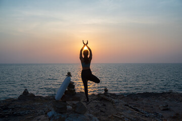 silhouette of Asian woman practicing yoga on the ocean coast with sea view .wellness, healthcare, sport and lifestyle concept .
