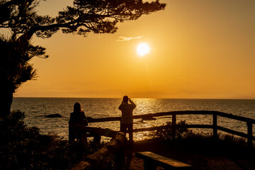 Fototapeta na wymiar 海に沈む夕日を眺めるカップルのシルエット　秋谷海岸　立石公園