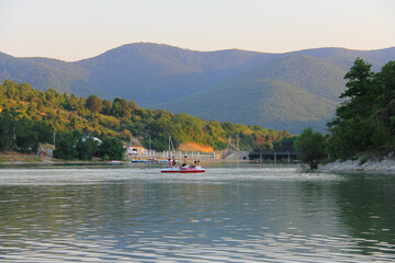 Fototapeta premium Summer landscape with a lake in the mountains - in the evening haze and setting sun after a hot June day.