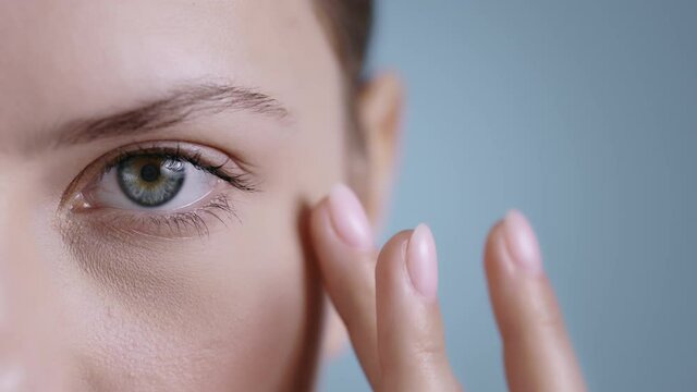 Close up view of beautiful young woman touching face half and looking to camera . Portrait of pretty female person with light nude make up posing at studio background.