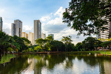 Paisagem com prédios e árvores, com reflexo na água do lago. Foto feita no Parque Flamboyant.