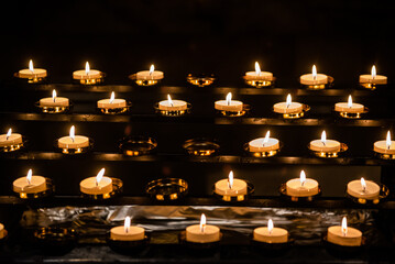 Vigil candles are lit in a church. - obrazy, fototapety, plakaty