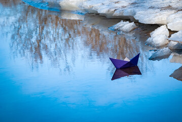 A colorful paper ship sails in the lake. It's got ice and snow around it.