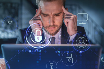Handsome businessman in suit at workplace working with laptop to defend customer cyber security. Concept of clients information protection and brainstorm. Padlock hologram over office background.