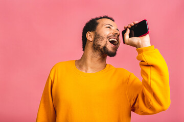 Listening cool music. Young cheerful african american black man moving dancing and singing isolated over pink background.
