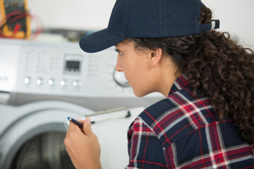 Naklejka na ściany i meble servicewoman with clipboard looking at washing machine