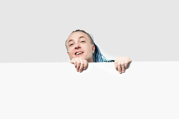 A young man with an interesting mohawk hairstyle peeks out from above a white wall. There is space...