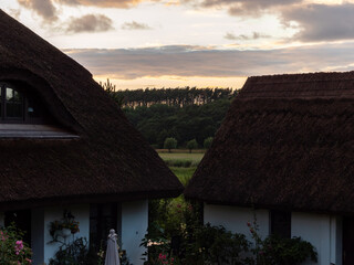 Beautiful sunset sky behind two houses with thatched roofs. Idyllic nature on Rügen island in Germany. Rural scene in the evening.