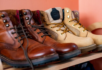 A close up of men’s brown brogue lace up boots on a wooden shoe rack with intentional selective focus, shallow depth of field and bokeh.