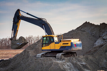 Large construction excavator yellow on a construction site in a quarry for quarrying. Yellow excavator on a construction site against blue sky.