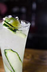 white cocktail with cucumber and ice in a bar at night