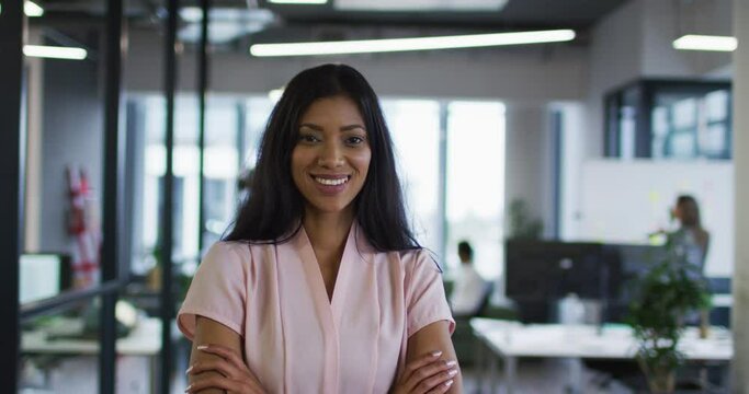 Portrait of mixed race businesswoman standing in office with arms crossed smiling to camera