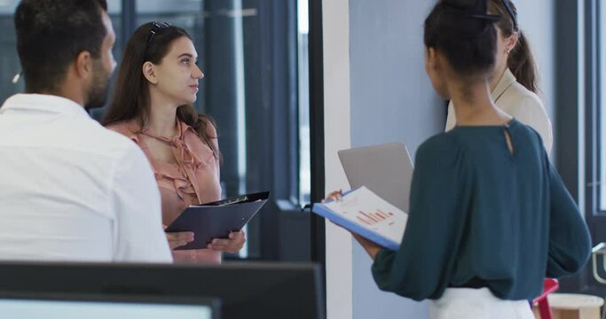 Caucasian businesswoman holding file talking to diverse colleagues at casual office meeting